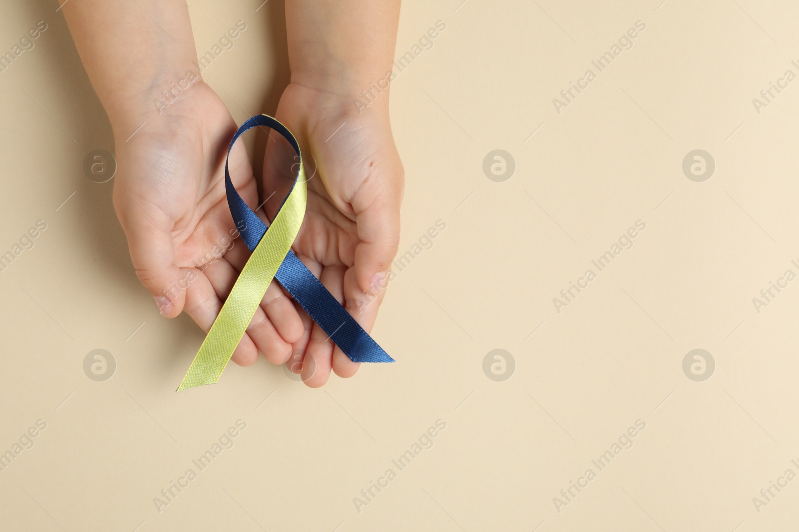 Photo of Child with yellow and blue ribbon on beige background, top view. Down syndrome awareness