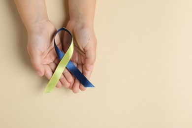 Photo of Child with yellow and blue ribbon on beige background, top view. Down syndrome awareness