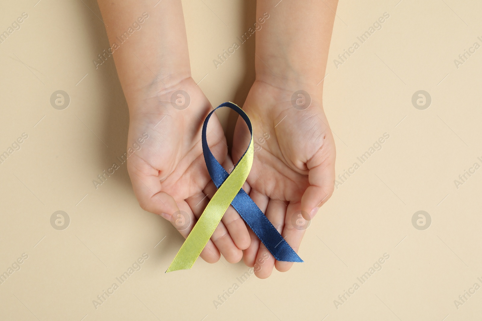 Photo of Child with yellow and blue ribbon on beige background, top view. Down syndrome awareness