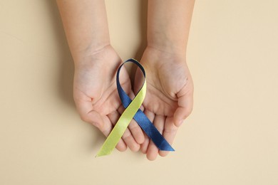 Photo of Child with yellow and blue ribbon on beige background, top view. Down syndrome awareness