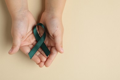 Photo of Child with teal ribbon on beige background, top view and space for text. Ovarian cancer and gynecological disorders awareness