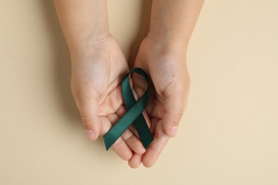 Photo of Child with teal ribbon on beige background, top view. Ovarian cancer and gynecological disorders awareness