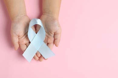 Photo of Child with light blue ribbon on pink background, top view and space for text. Childhood cancer awareness