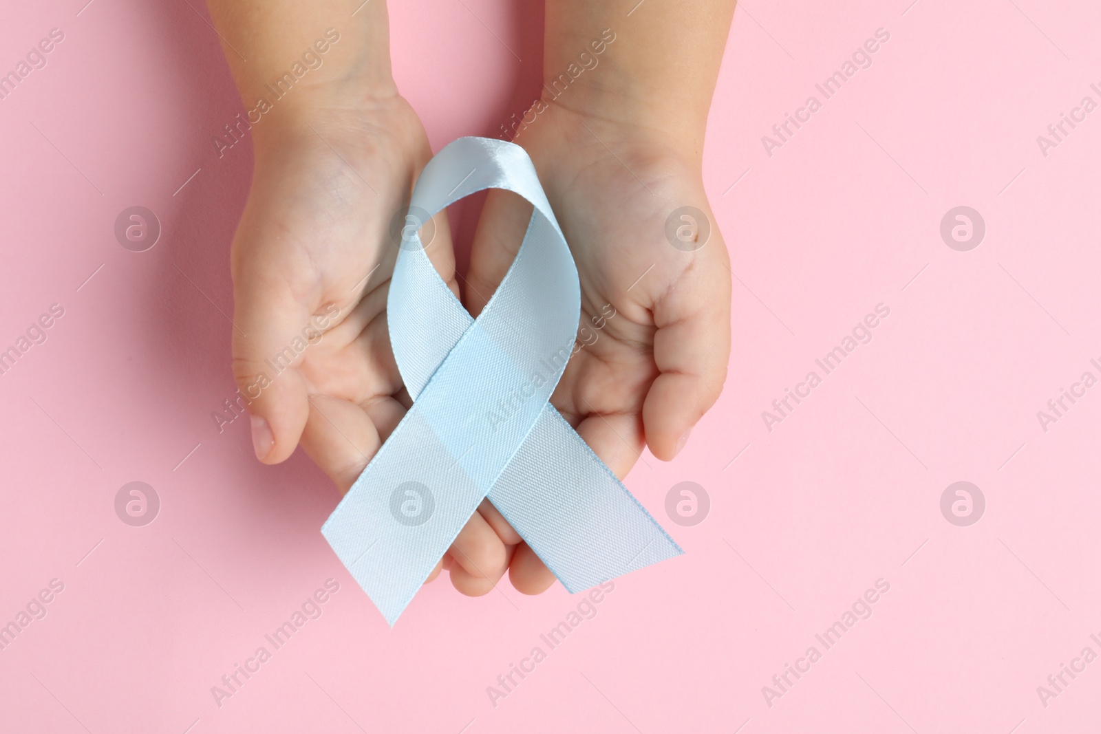 Photo of Child with light blue ribbon on pink background, top view. Childhood cancer awareness