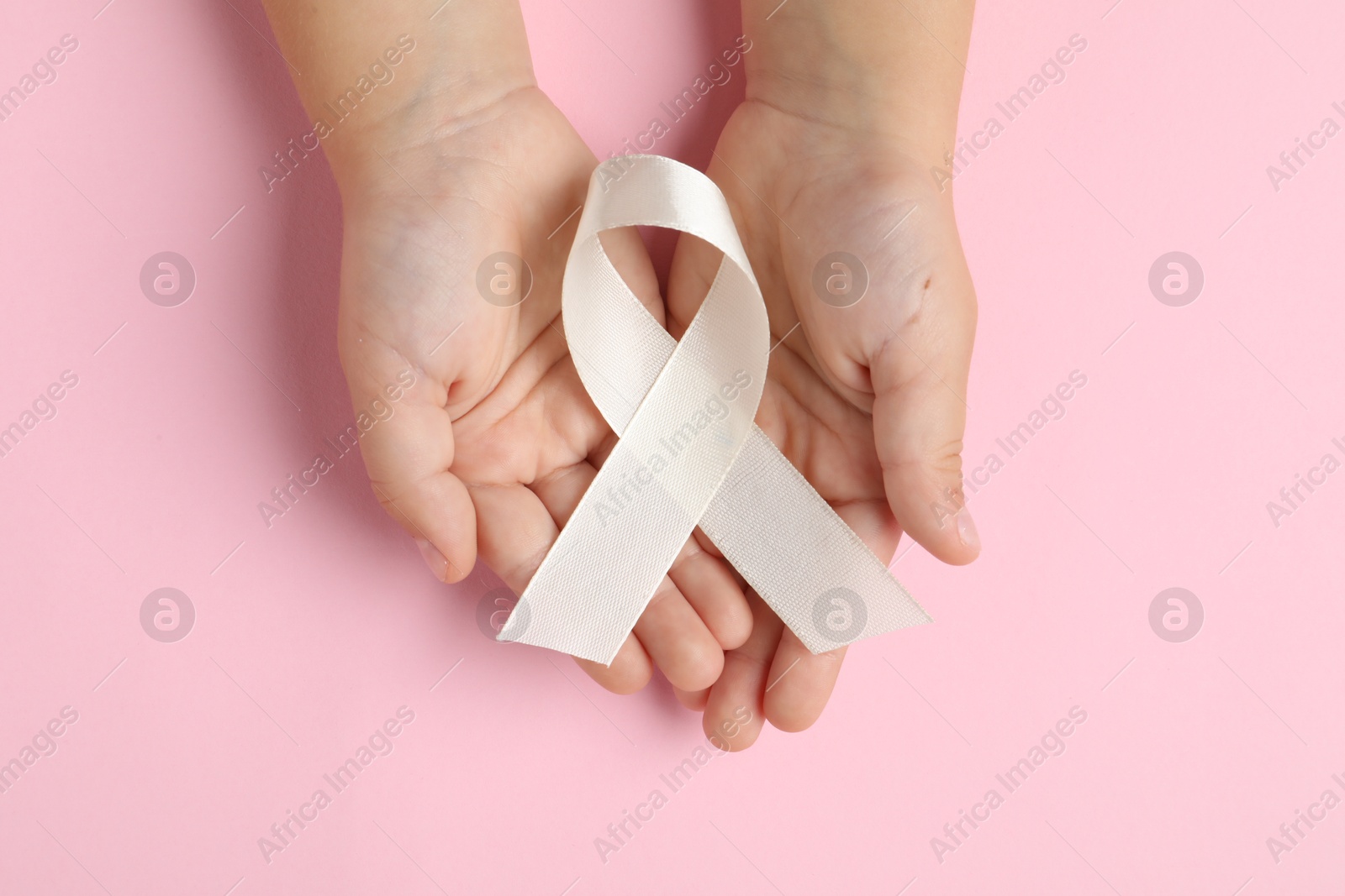 Photo of Child with white ribbon on pink background, top view. Bone cancer and lung disease awareness