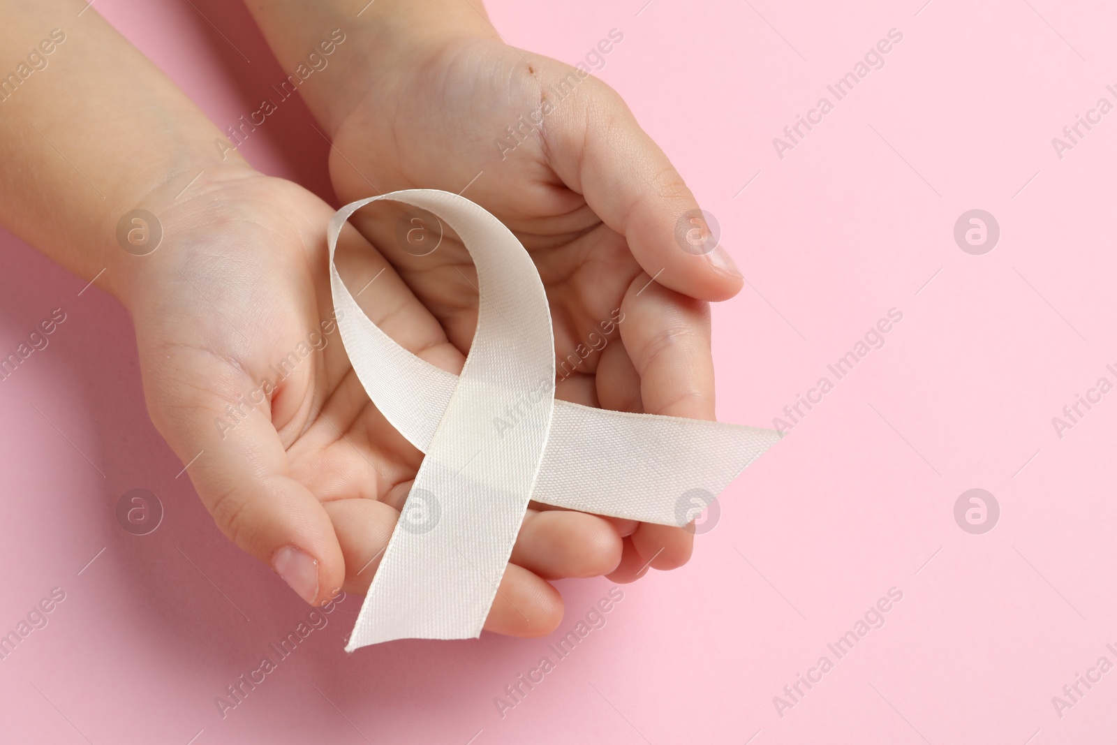 Photo of Child with white ribbon on pink background, closeup and space for text. Bone cancer and lung disease awareness