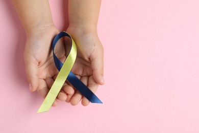 Photo of Child with yellow and blue ribbon on pink background, top view. Down syndrome awareness