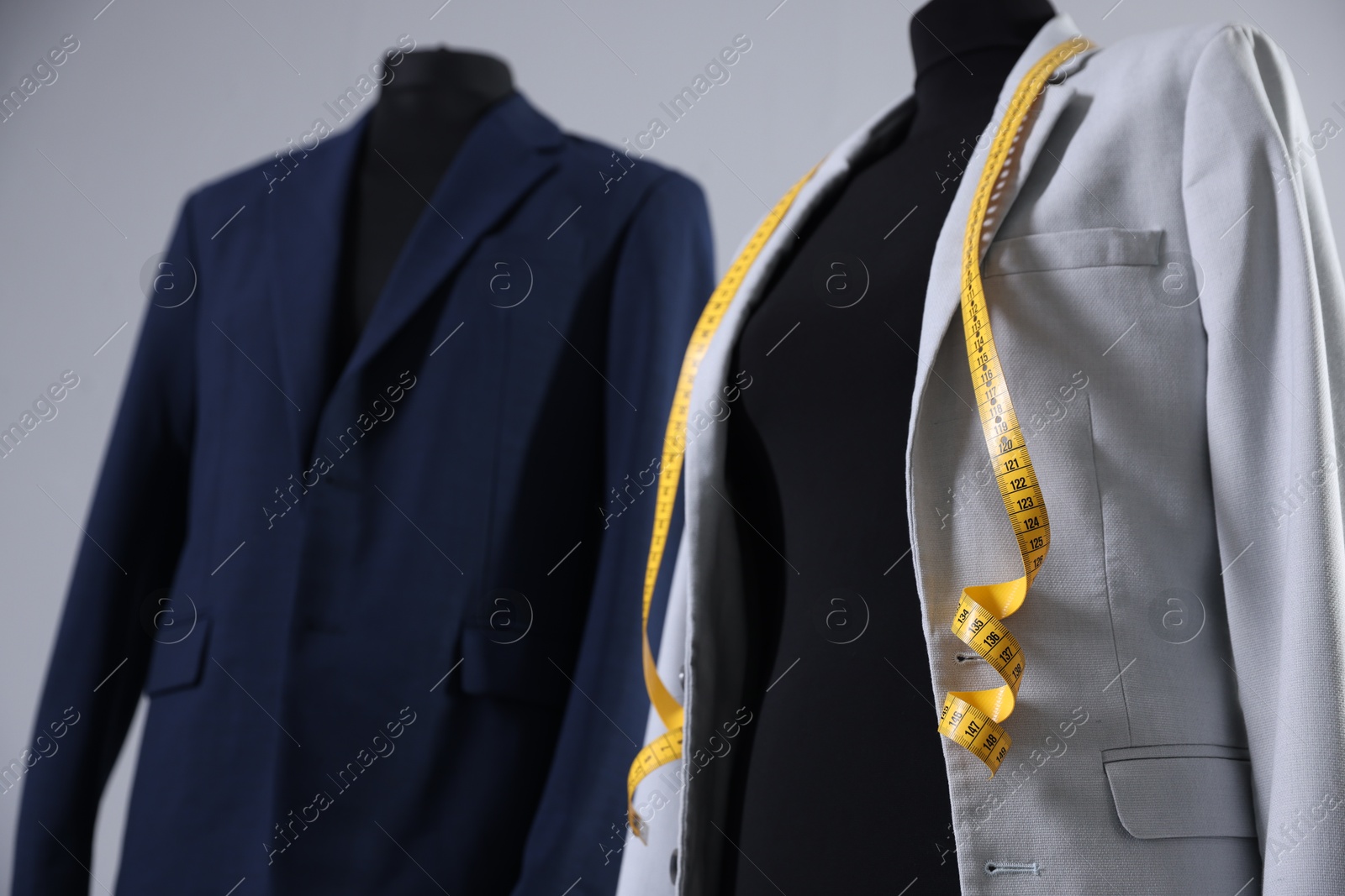 Photo of Mannequins with jackets and measuring tape on gray background, closeup