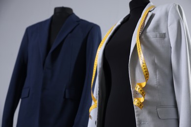 Photo of Mannequins with jackets and measuring tape on gray background, closeup