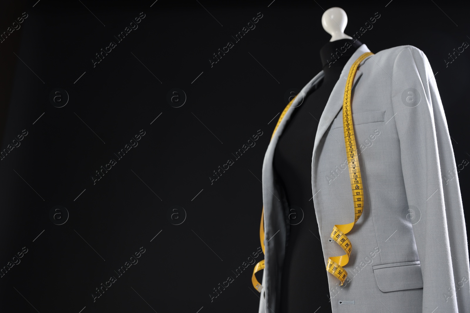 Photo of Female mannequin with gray jacket and measuring tape on dark background, space for text