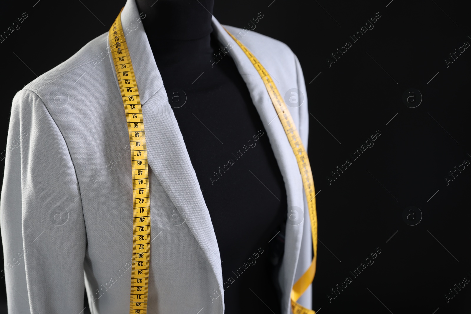 Photo of Female mannequin with gray jacket and measuring tape on black background, closeup. Space for text