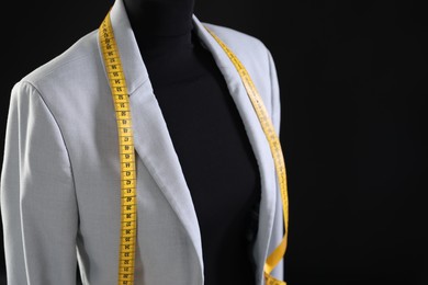 Female mannequin with gray jacket and measuring tape on black background, closeup. Space for text