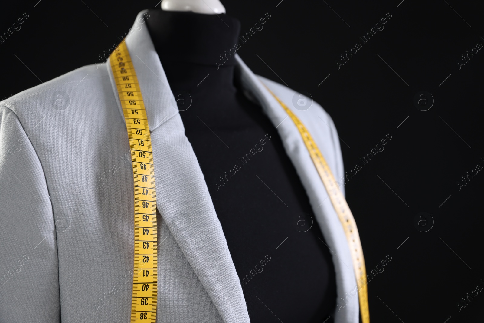 Photo of Female mannequin with gray jacket and measuring tape on black background, closeup