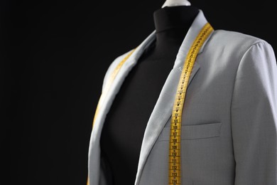 Photo of Female mannequin with gray jacket and measuring tape on black background, closeup. Space for text