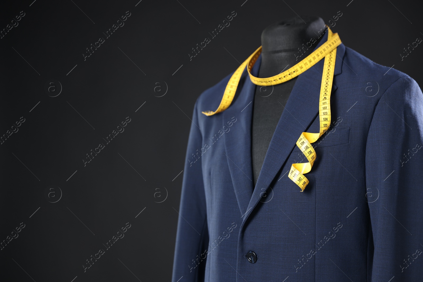 Photo of Male mannequin with jacket and measuring tape on dark background, closeup. Space for text