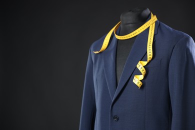 Male mannequin with jacket and measuring tape on dark background, closeup. Space for text