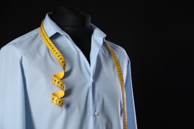 Male mannequin with shirt and measuring tape on black background, closeup