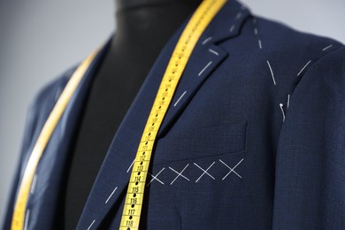 Semi-ready jacket and measuring tape on mannequin against gray background, closeup