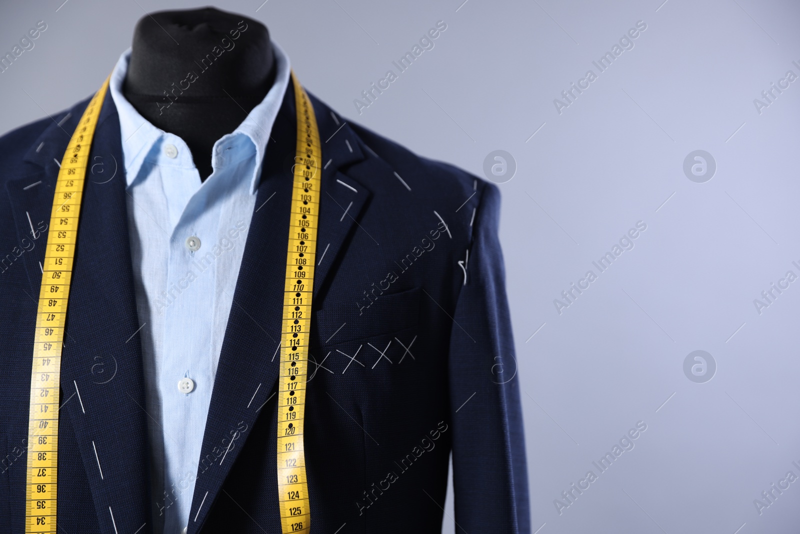 Photo of Semi-ready jacket, shirt and measuring tape on mannequin against gray background, closeup. Space for text