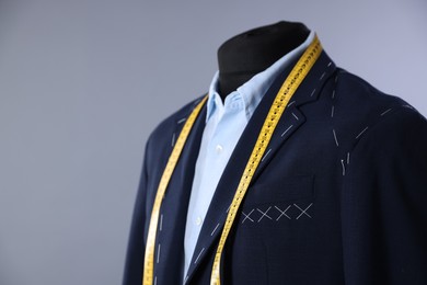 Semi-ready jacket, shirt and measuring tape on mannequin against gray background, closeup. Space for text