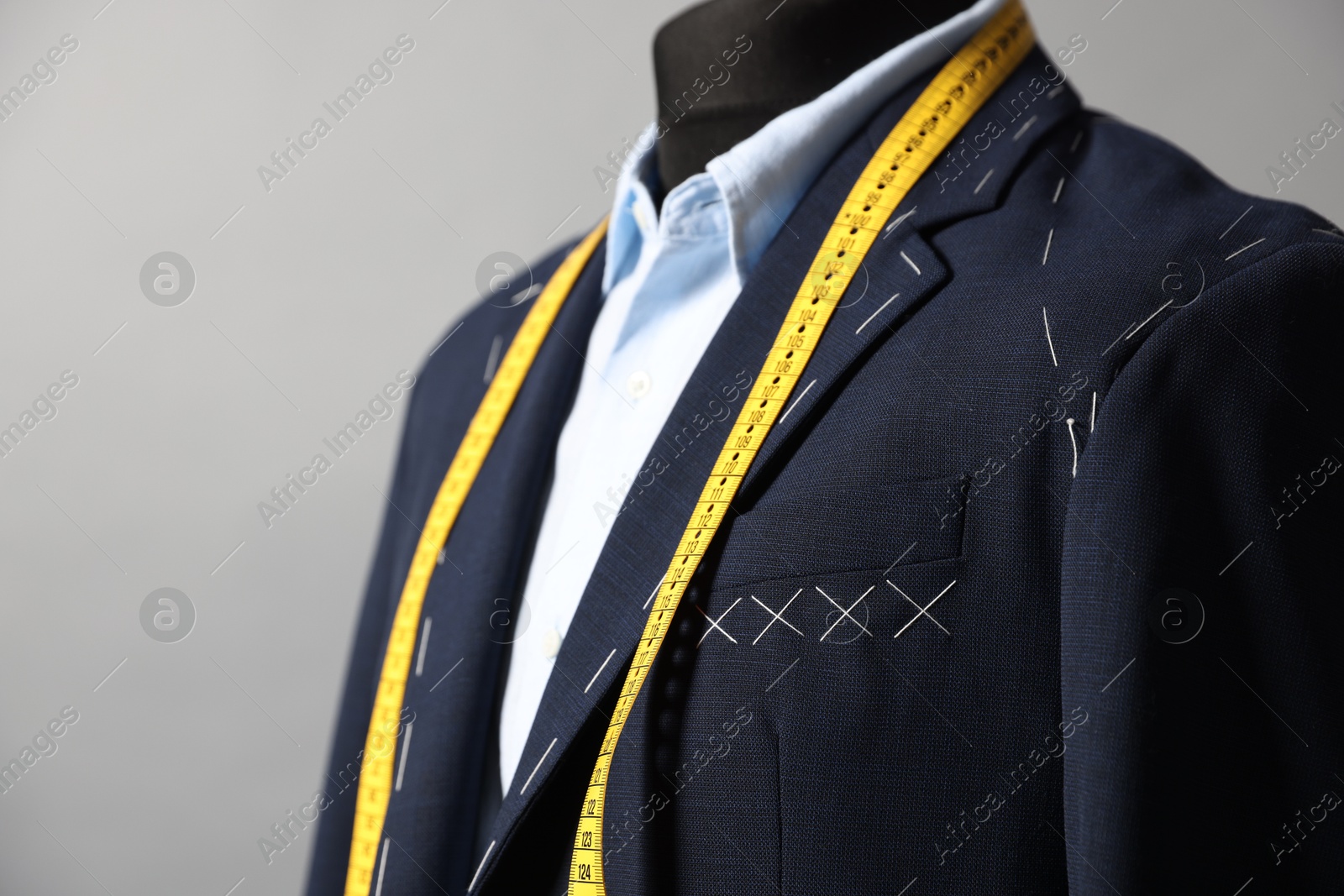 Photo of Semi-ready jacket, shirt and measuring tape on mannequin against gray background, closeup