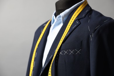 Semi-ready jacket, shirt and measuring tape on mannequin against gray background, closeup