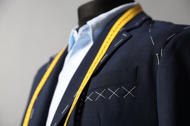 Photo of Semi-ready jacket, shirt and measuring tape on mannequin against gray background, closeup