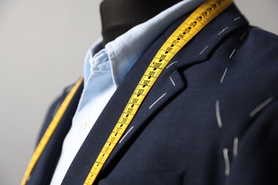 Semi-ready jacket, shirt and measuring tape on mannequin against gray background, closeup