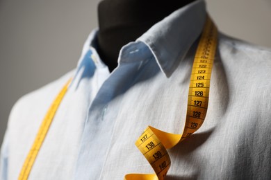 Male mannequin with shirt and measuring tape on gray background, closeup