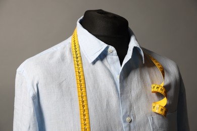 Male mannequin with shirt and measuring tape on gray background, closeup