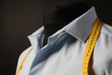 Male mannequin with shirt and measuring tape on dark background, closeup