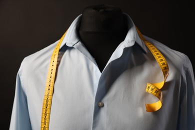 Male mannequin with shirt and measuring tape on dark background, closeup