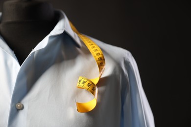 Male mannequin with shirt and measuring tape on dark background, closeup