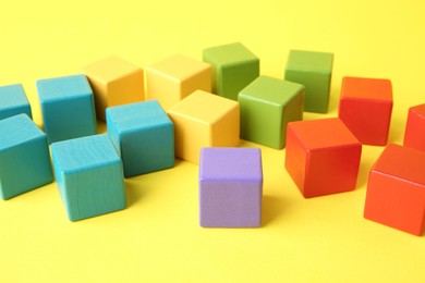 Photo of Many wooden colorful cubes on yellow background, closeup