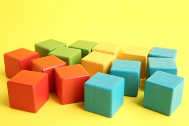 Photo of Many wooden colorful cubes on yellow background, closeup