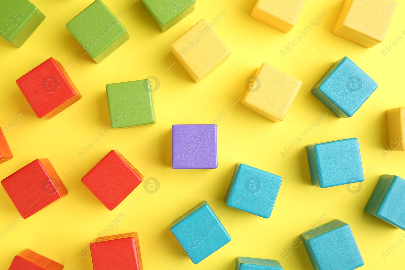 Photo of Many wooden colorful cubes on yellow background, flat lay