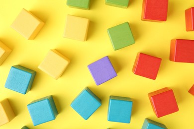 Photo of Many wooden colorful cubes on yellow background, flat lay