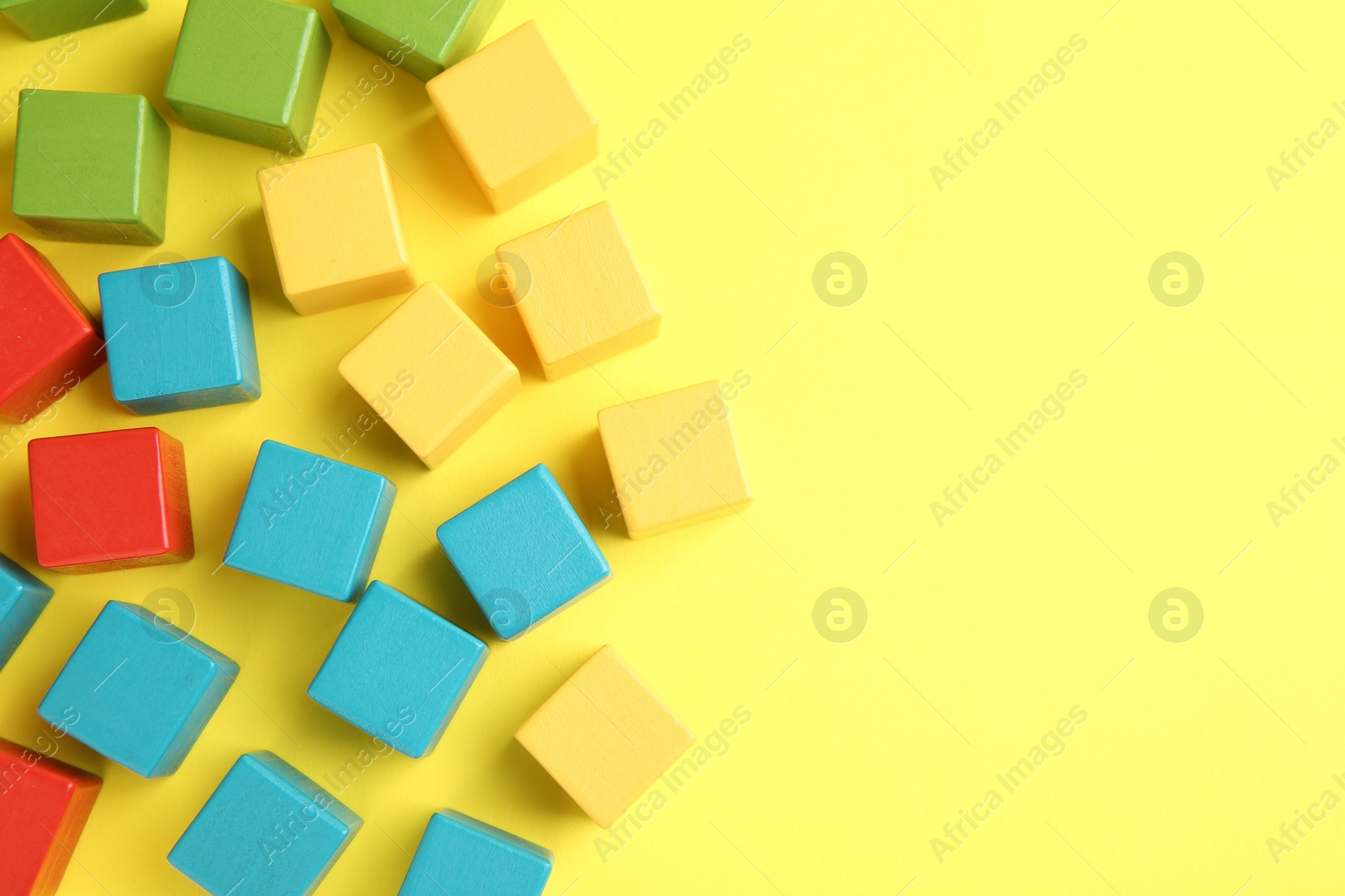 Photo of Many wooden colorful cubes on yellow background, flat lay. Space for text