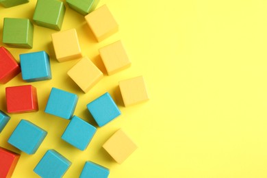 Photo of Many wooden colorful cubes on yellow background, flat lay. Space for text