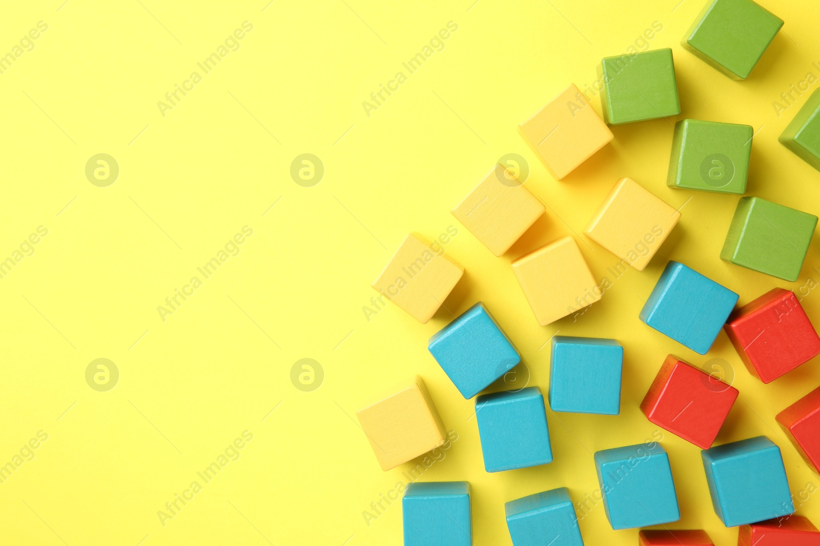 Photo of Many wooden colorful cubes on yellow background, flat lay. Space for text