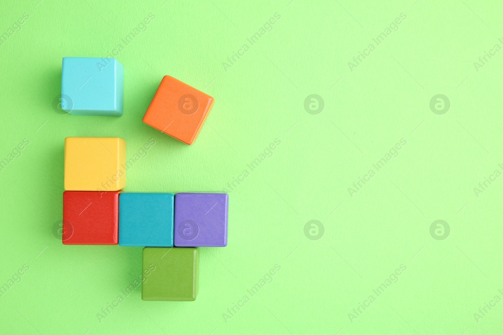 Photo of Many wooden colorful cubes on green background, top view. Space for text