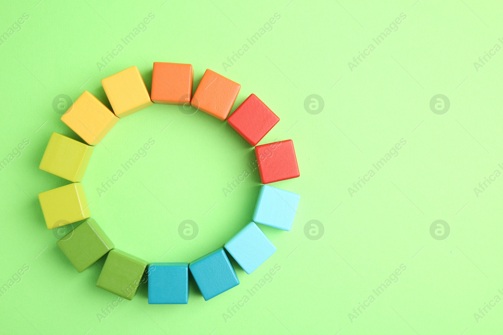 Photo of Many wooden colorful cubes on green background, top view. Space for text