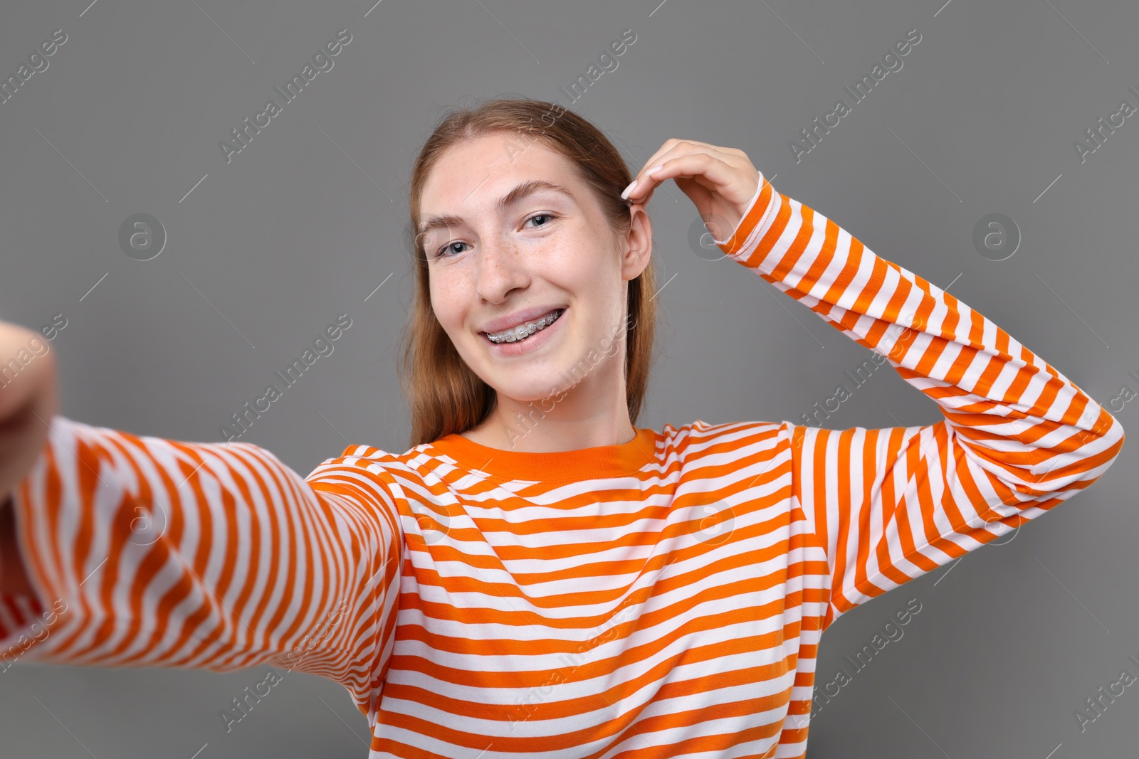 Photo of Smiling girl with braces taking selfie on grey background