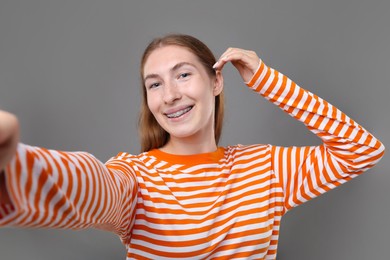 Photo of Smiling girl with braces taking selfie on grey background