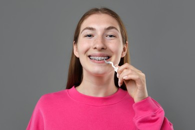 Photo of Smiling girl with braces cleaning teeth with interdental brush on grey background