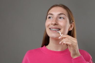 Photo of Smiling girl with braces cleaning teeth with interdental brush on grey background