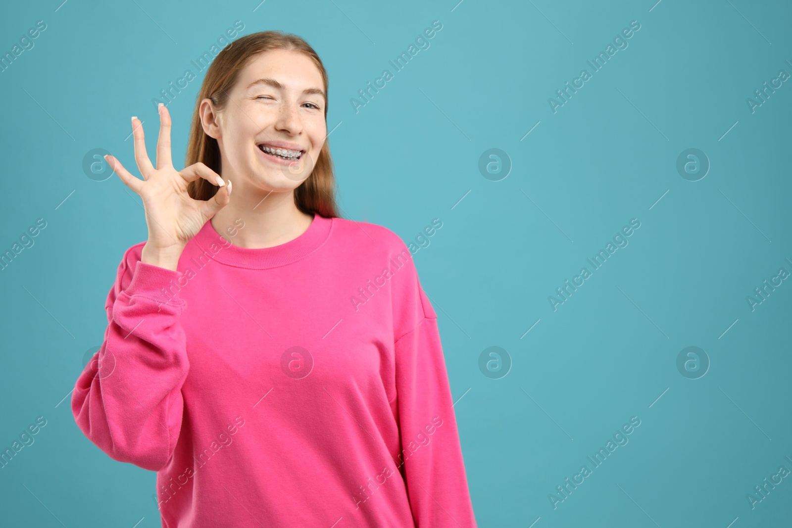 Photo of Smiling girl with braces showing ok gesture on light blue background, space for text