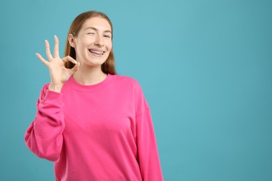 Photo of Smiling girl with braces showing ok gesture on light blue background, space for text