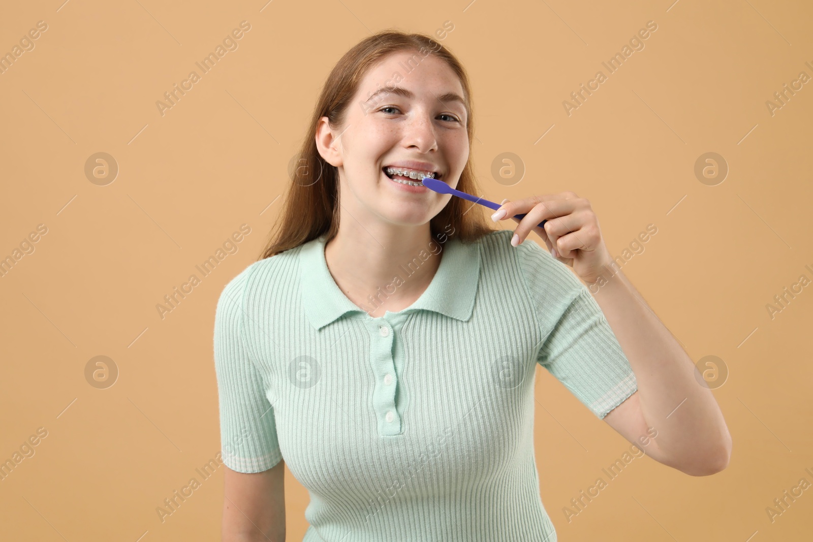 Photo of Girl with braces cleaning teeth on beige background