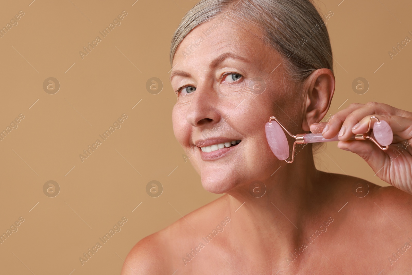 Photo of Beautiful woman doing facial massage with roller on beige background